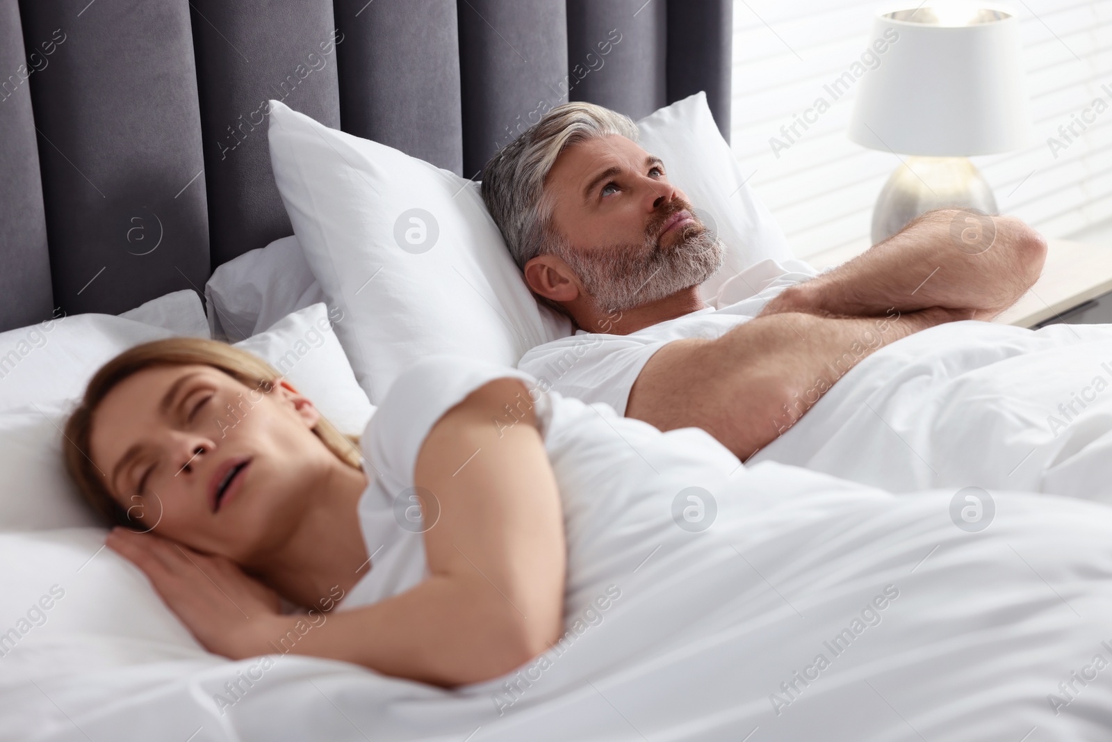 Photo of Irritated man lying near his snoring wife in bed at home