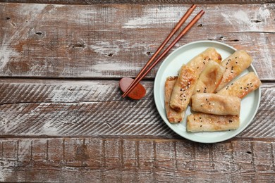 Photo of Tasty fried spring rolls served on wooden table, flat lay. Space for text