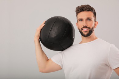 Athletic man with medicine ball on light grey background