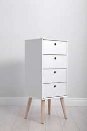 Photo of Stylish chest of drawers near white wall. Furniture for wardrobe room