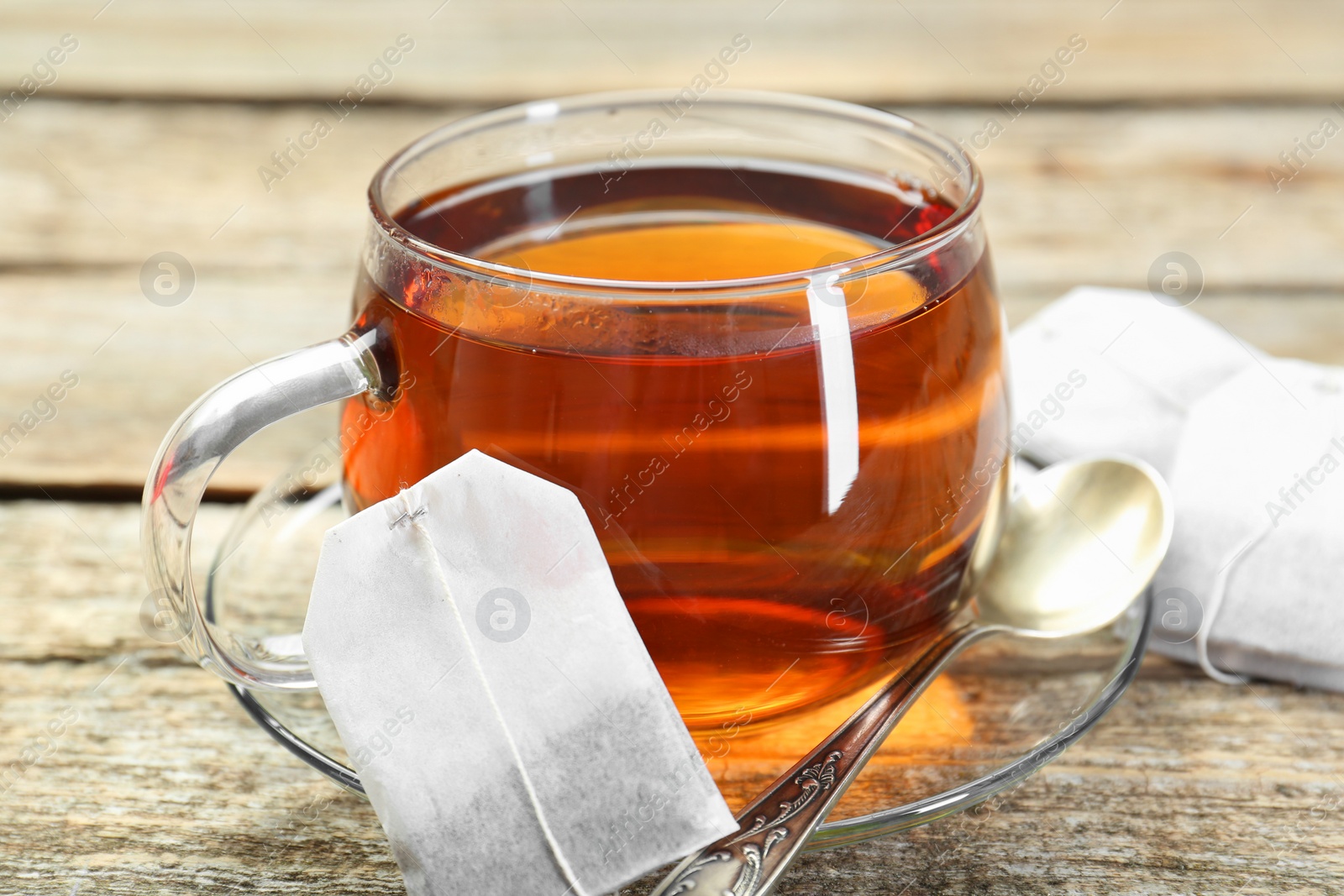 Photo of Aromatic tea in glass cup, spoon and teabags on wooden table