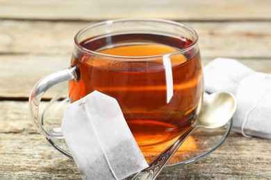 Photo of Aromatic tea in glass cup, spoon and teabags on wooden table