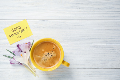 Delicious coffee, flowers and card with GOOD MORNING wish on white wooden table, flat lay. Space for text