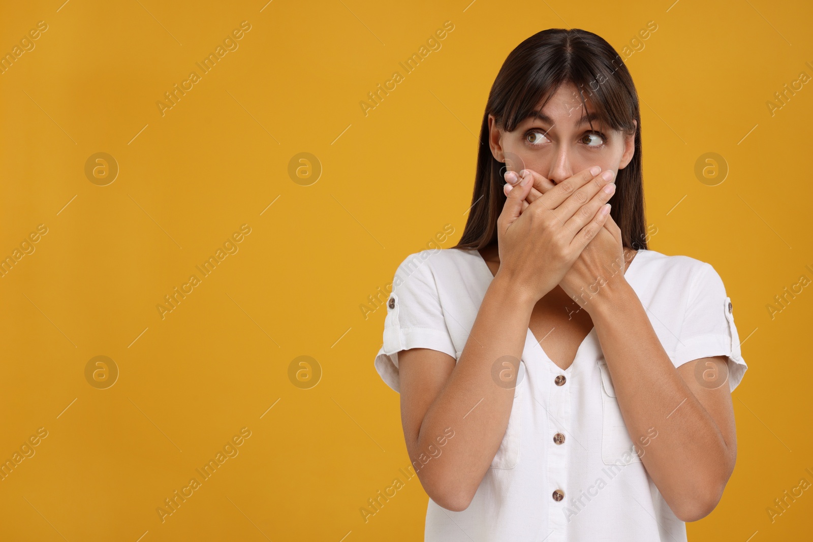 Photo of Embarrassed woman covering mouth with hands on orange background, space for text