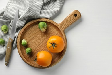 Cutting board with Brussels sprouts, tomatoes and knife on white wooden table, flat lay. Space for text