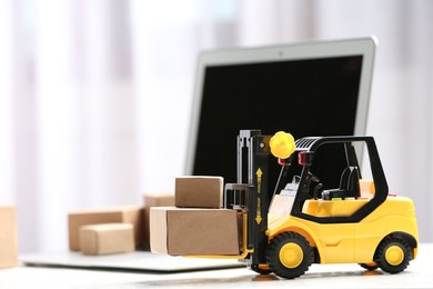 Photo of Toy forklift with boxes near laptop on table. Logistics and wholesale concept