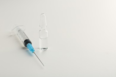 Photo of Glass ampoule with liquid and syringe on white background. Space for text