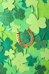 Photo of St. Patrick's day. Golden horseshoe and decorative clover leaves on green background, flat lay