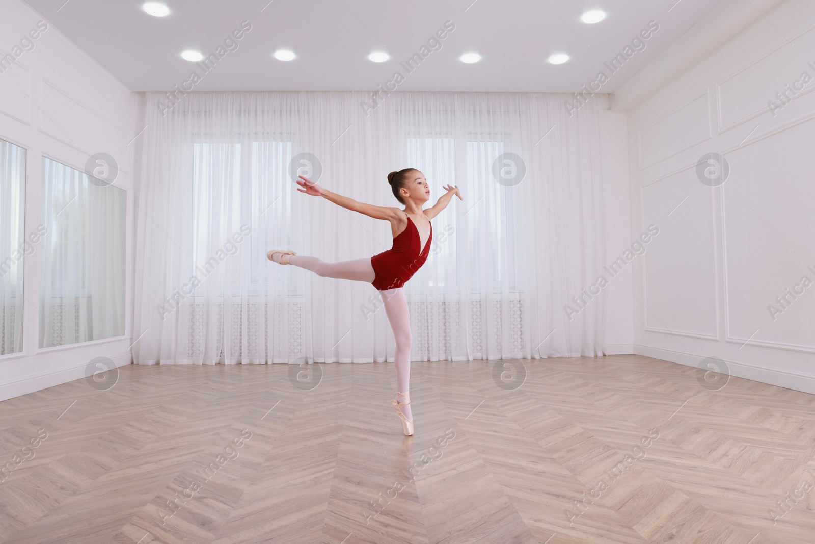 Photo of Little ballerina practicing dance moves in studio