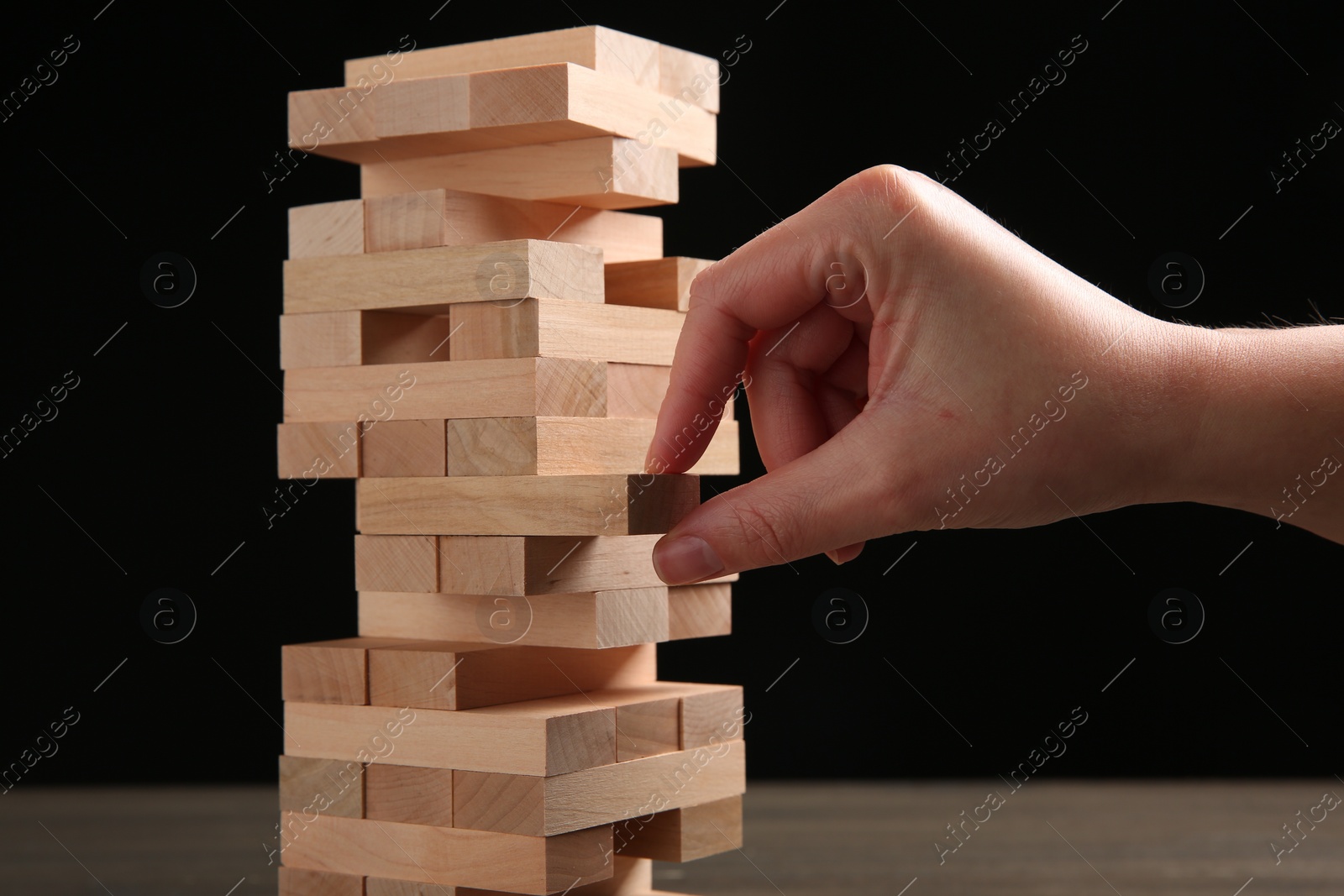 Photo of Woman playing Jenga at table against black background, closeup