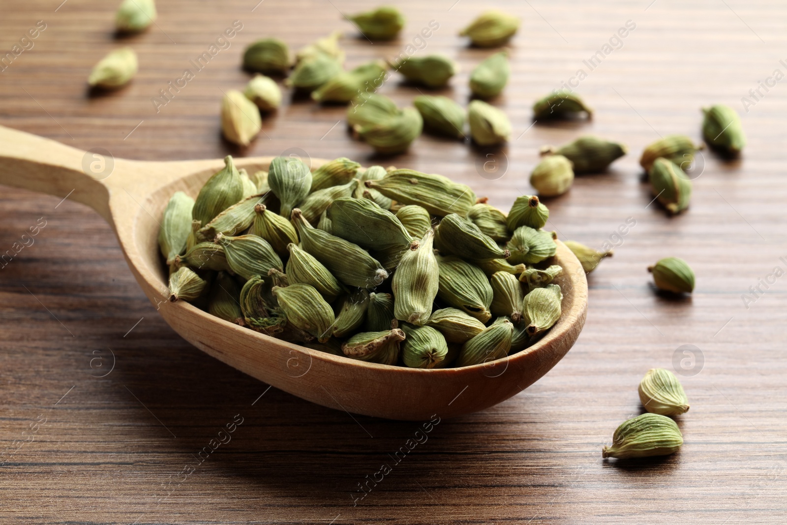 Photo of Spoon with dry cardamom pods on wooden table, closeup