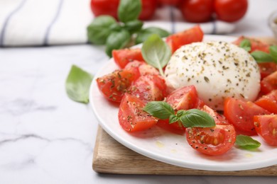 Photo of Tasty salad Caprese with mozarella, tomatoes and basil on white marble table, closeup