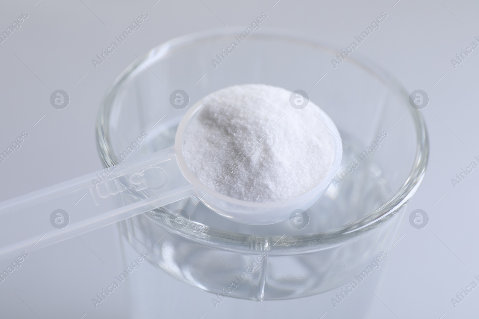 Photo of Spoon with baking soda over glass of water on light grey background, closeup