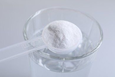 Photo of Spoon with baking soda over glass of water on light grey background, closeup