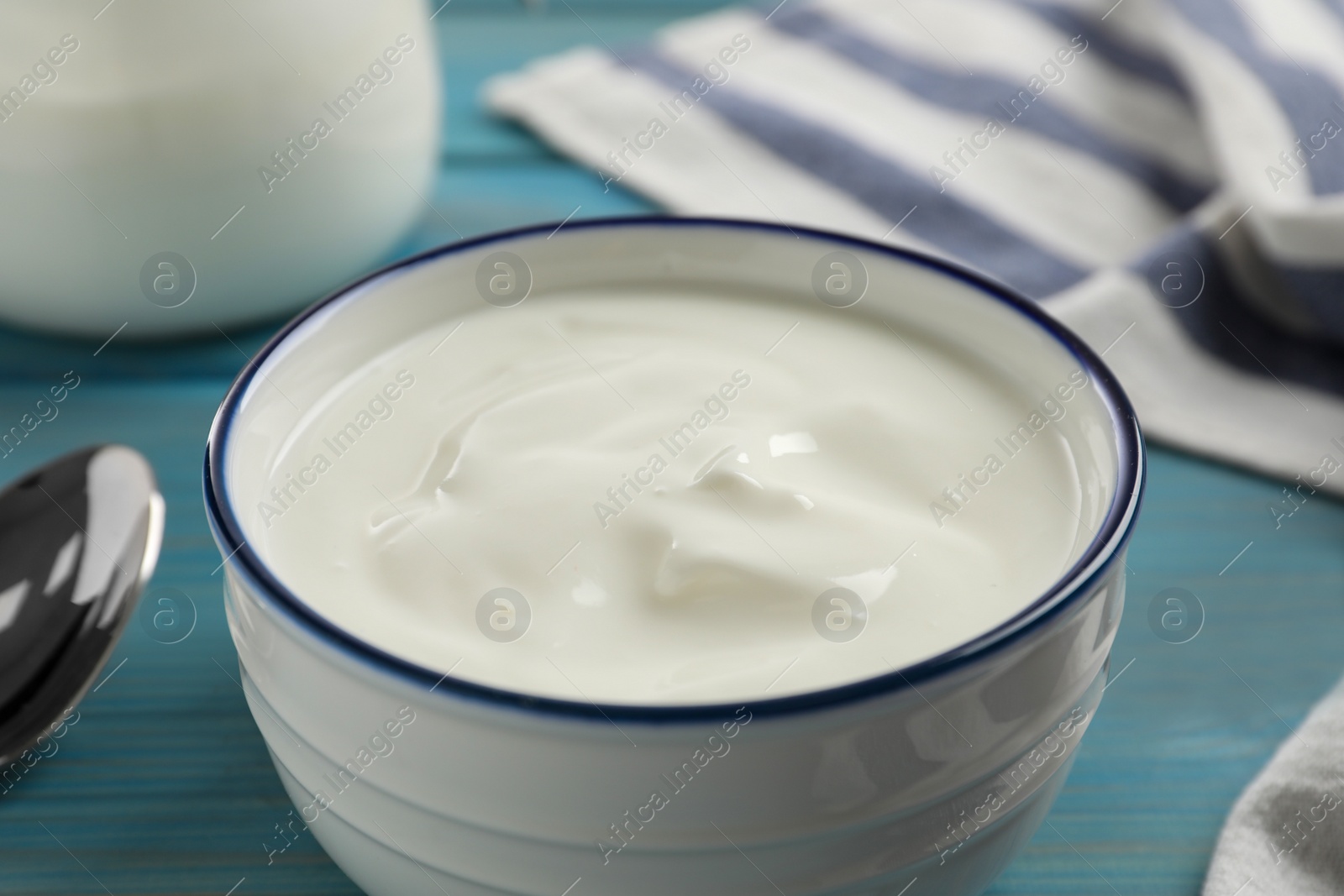 Photo of Bowl of tasty yogurt on light blue wooden table, closeup