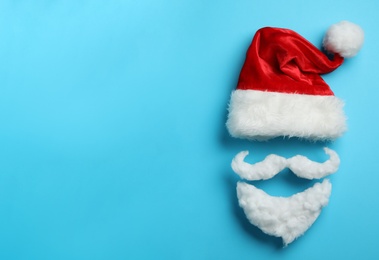 Photo of Santa Claus hat and beard on light blue background, flat lay. Space for text