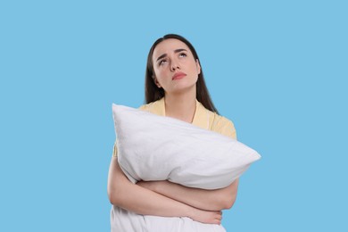 Photo of Tired young woman with pillow on light blue background. Insomnia problem