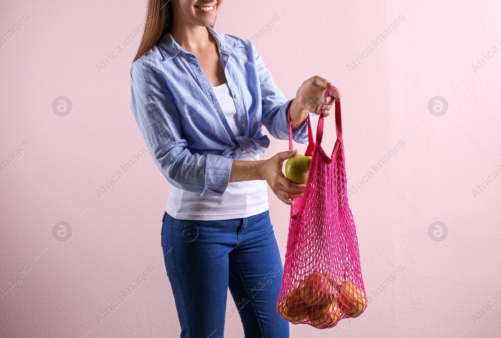 Photo of Woman holding net bag with fresh ripe pears on pink background, closeup