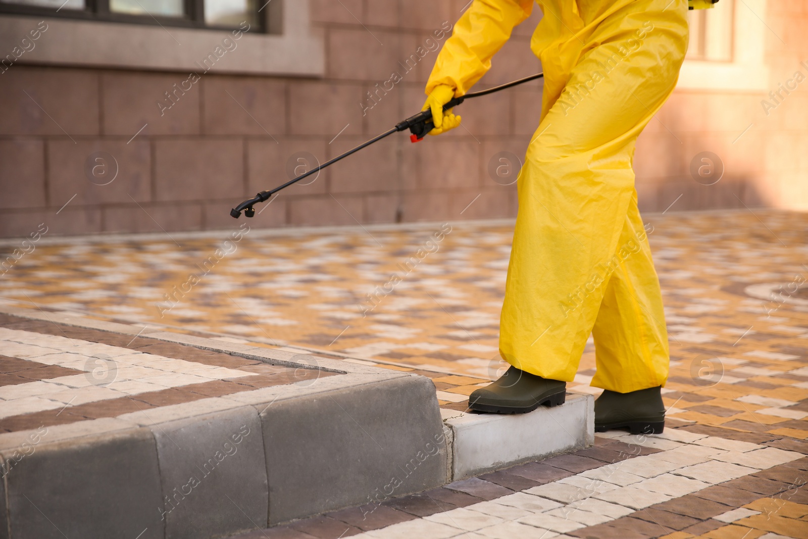 Photo of Person in hazmat suit disinfecting street with sprayer, closeup. Surface treatment during coronavirus pandemic