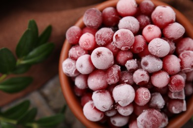 Photo of Frozen red cranberries in bowl and green leaves on table, top view