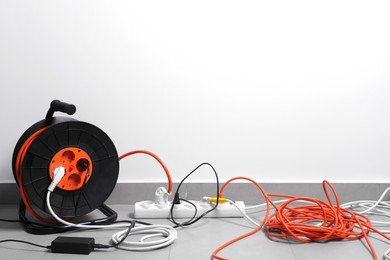 Extension cord reel plugged into power strip on grey floor indoors, space for text
