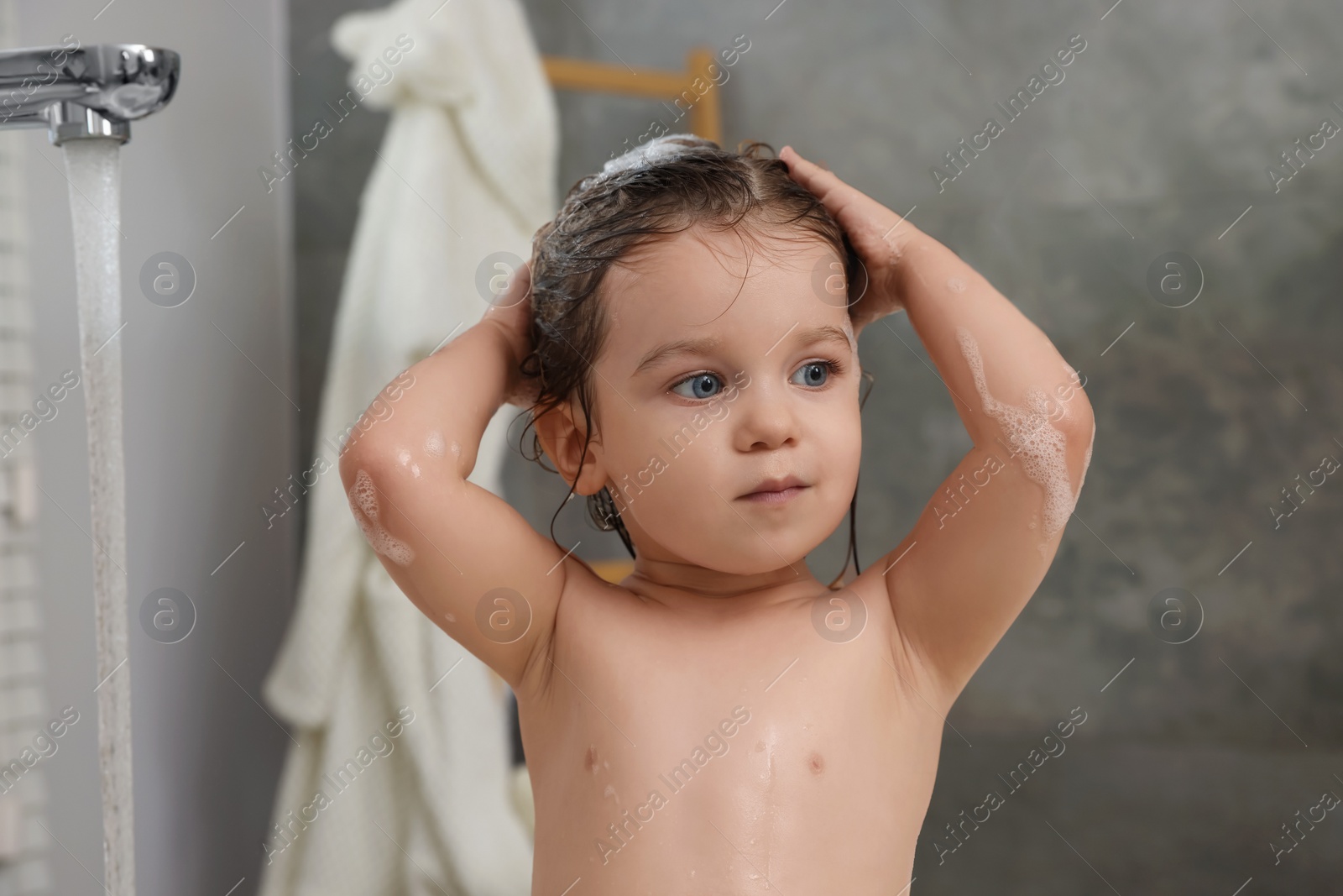 Photo of Cute little girl washing hair with shampoo in bathroom