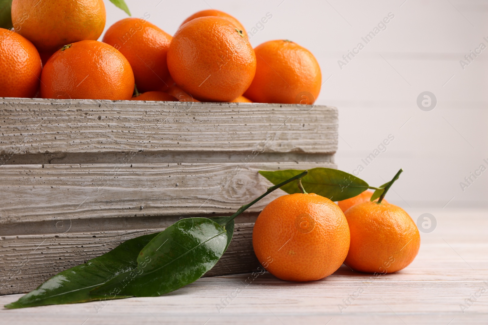 Photo of Delicious tangerines with leaves on light wooden table, closeup