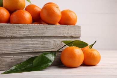 Delicious tangerines with leaves on light wooden table, closeup