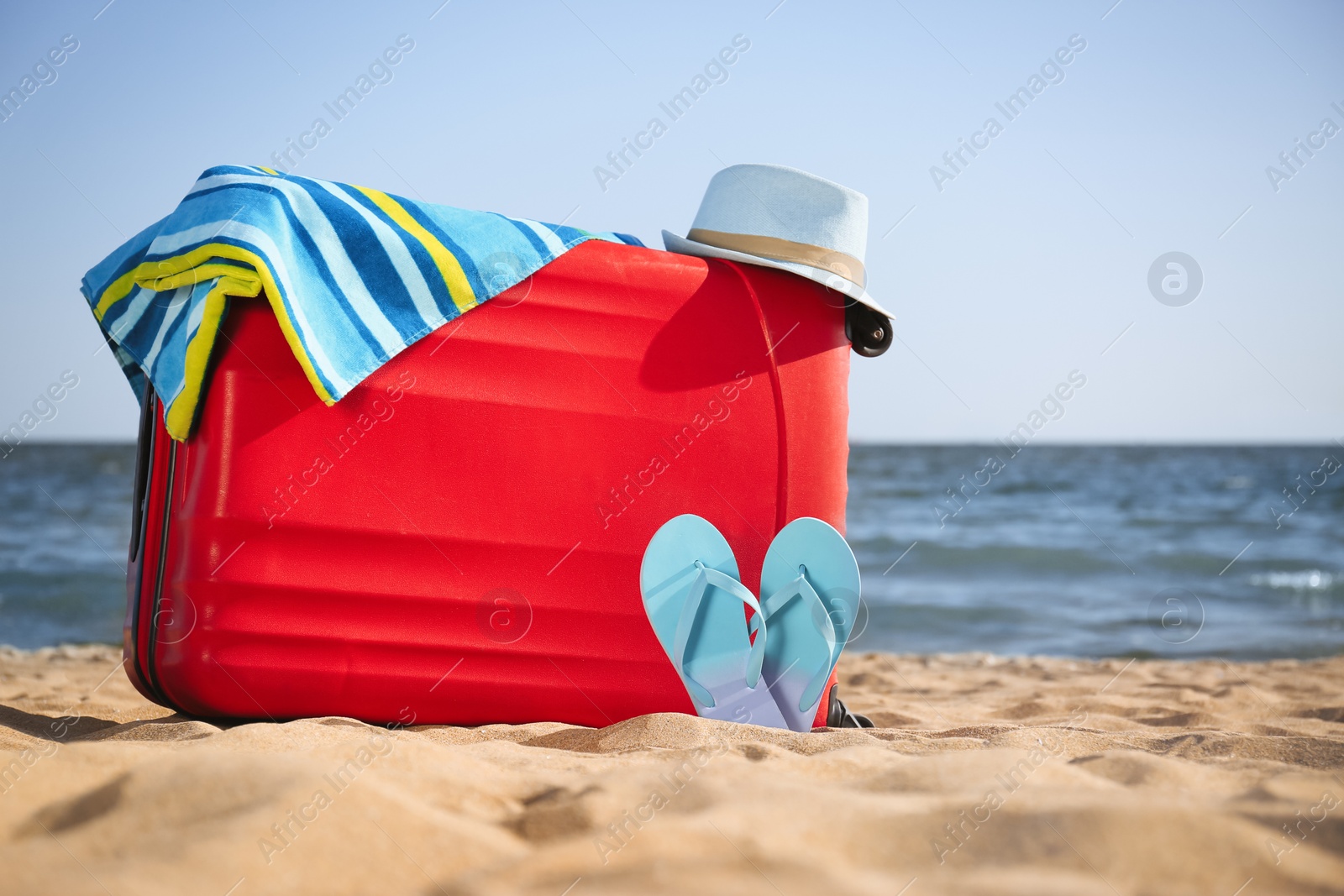 Photo of Bright suitcase and different beach accessories on sand near sea. Space for text