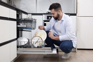 Photo of Man loading dishwasher with dirty plates indoors