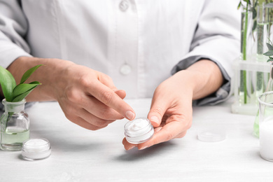 Photo of Woman with cream at table in cosmetic laboratory, closeup