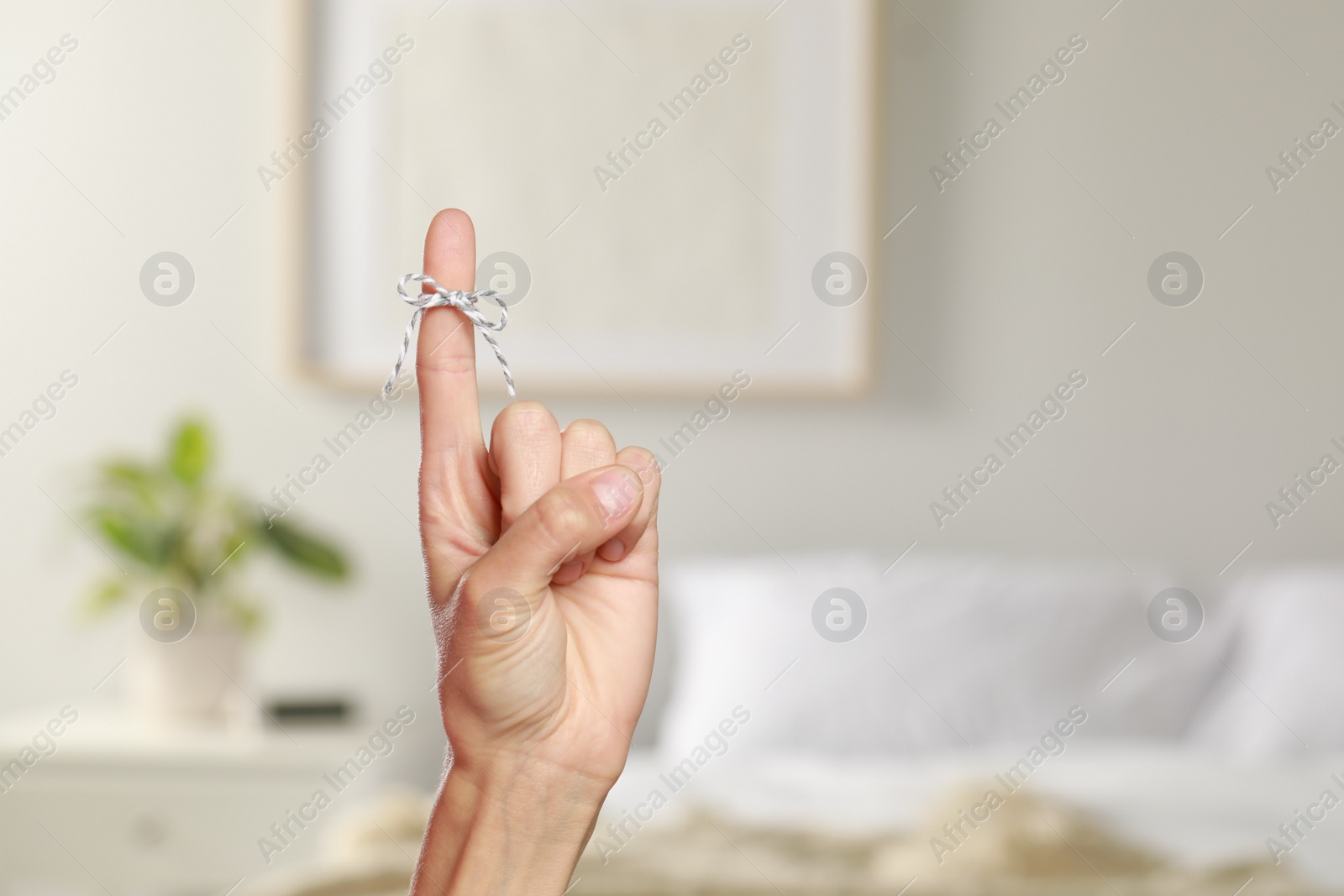 Photo of Woman showing index finger with tied bow as reminder indoors, closeup. Space for text