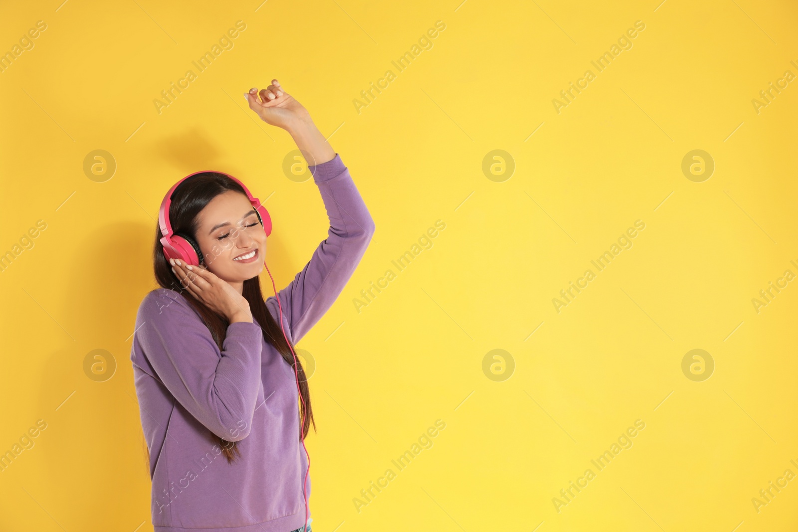 Photo of Attractive young woman enjoying music in headphones on color background. Space for text