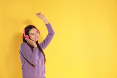 Photo of Attractive young woman enjoying music in headphones on color background. Space for text