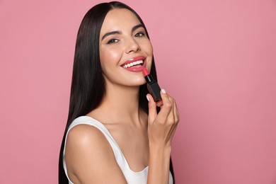 Young woman with beautiful makeup holding glossy lipstick on pink background