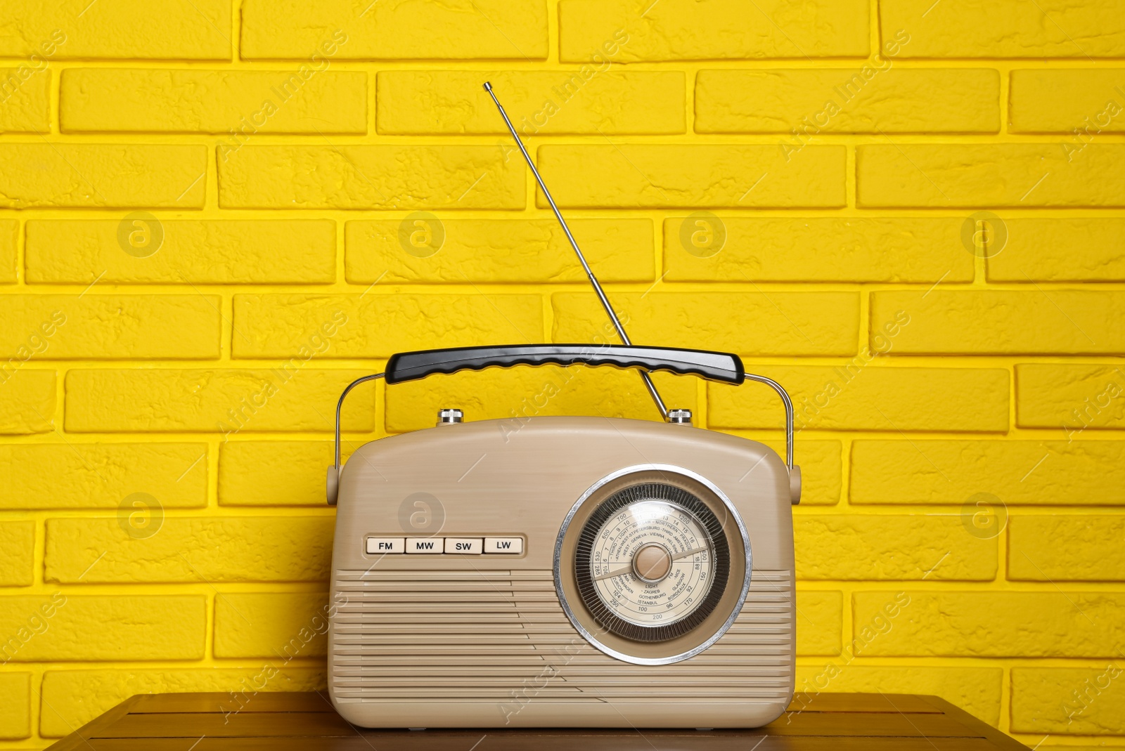 Photo of Retro radio receiver on wooden table near yellow brick wall