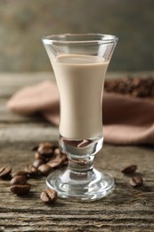 Coffee cream liqueur in glass and beans on wooden table, closeup