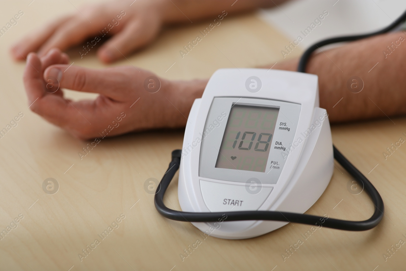 Photo of man checking blood pressure at wooden table indoors, closeup