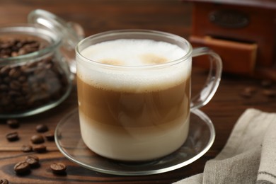 Aromatic coffee in cup and beans on wooden table, closeup