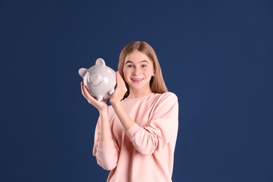 Teen girl with piggy bank on color background