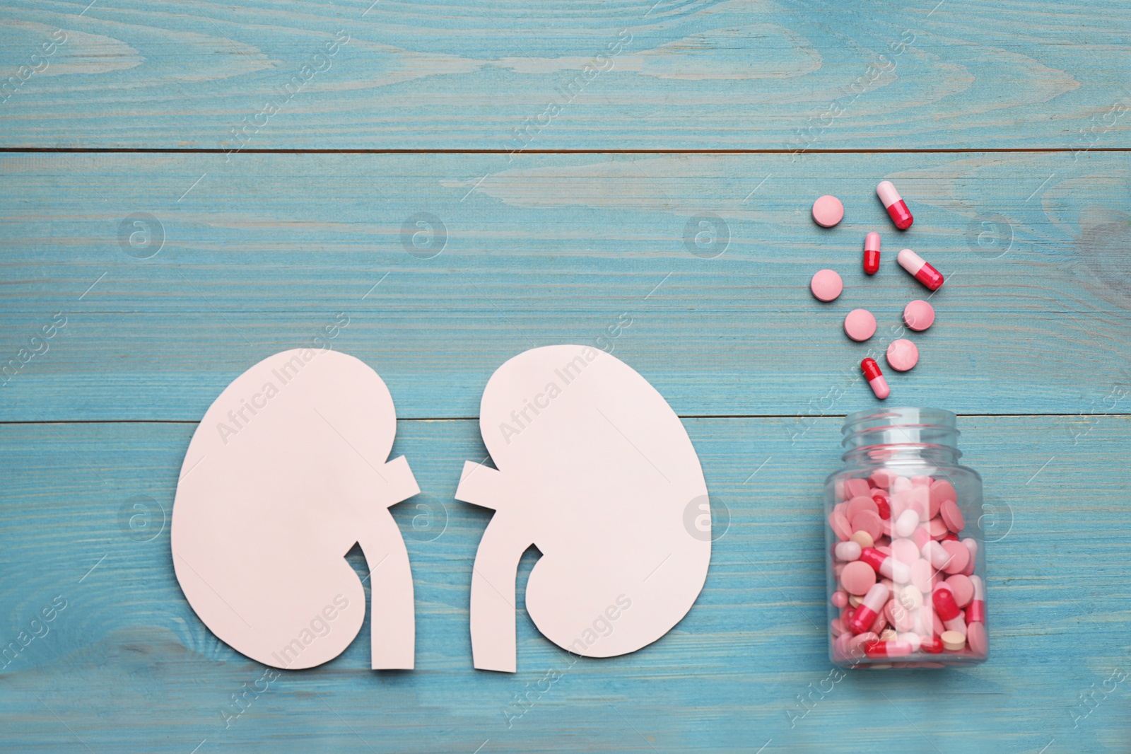 Photo of Paper cutout of kidneys and jar with pills on blue wooden table, flat lay