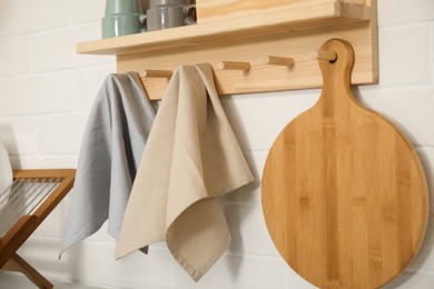 Photo of Different towels and wooden board hanging on rack in kitchen