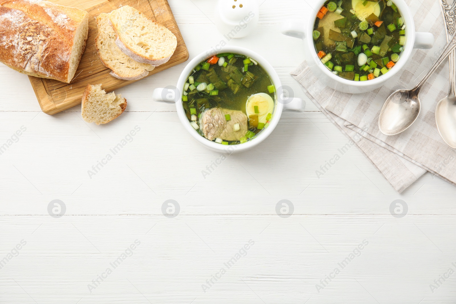 Photo of Delicious sorrel soup with meat and egg served on white wooden table, flat lay. Space for text