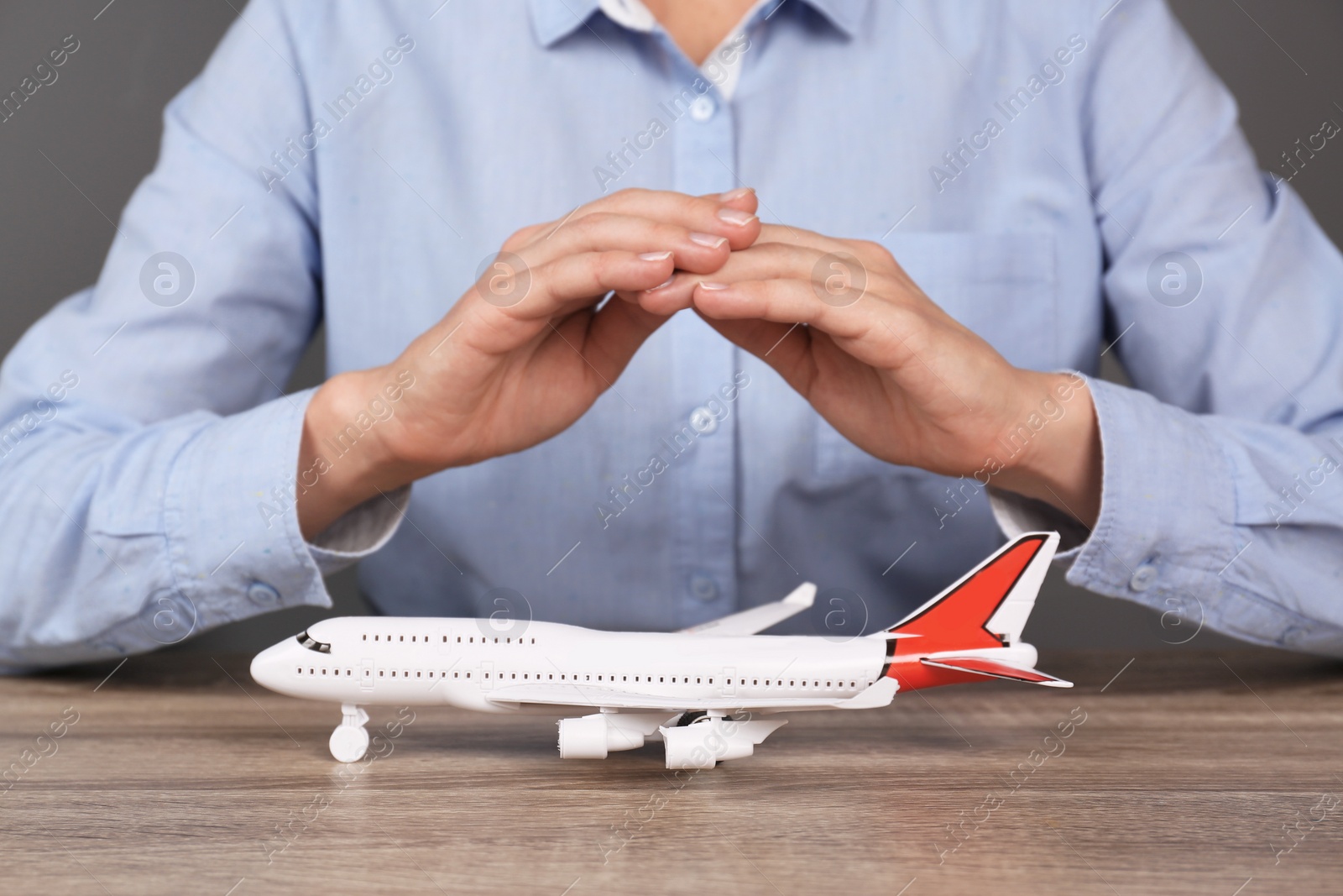 Photo of Insurance agent covering toy plane at table, closeup. Travel safety concept