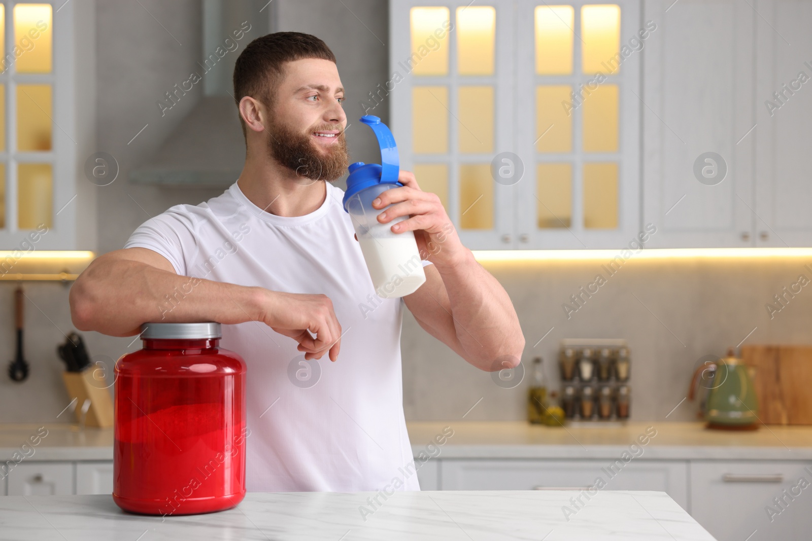 Photo of Young man with shaker of protein and powder at white marble table in kitchen