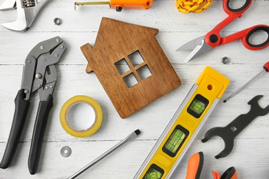 Photo of Set of repair tools and house figure on white wooden background, flat lay