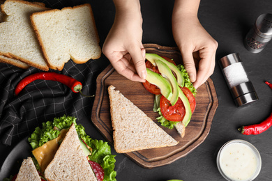 Photo of Woman making tasty sandwich with avocado at black table, top view