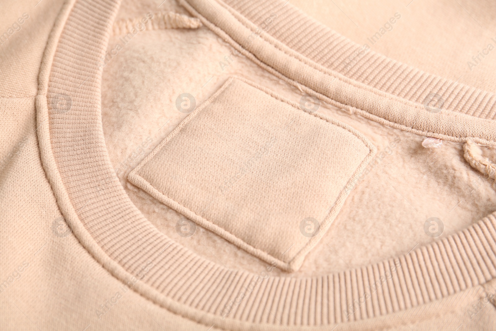 Photo of Blank clothing label on beige sweater, closeup