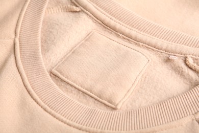 Photo of Blank clothing label on beige sweater, closeup