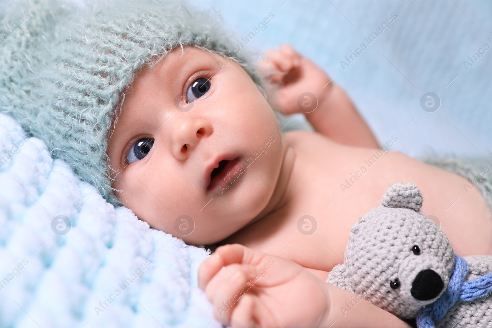 Photo of Cute newborn baby with crochet toy on light blue blanket, closeup